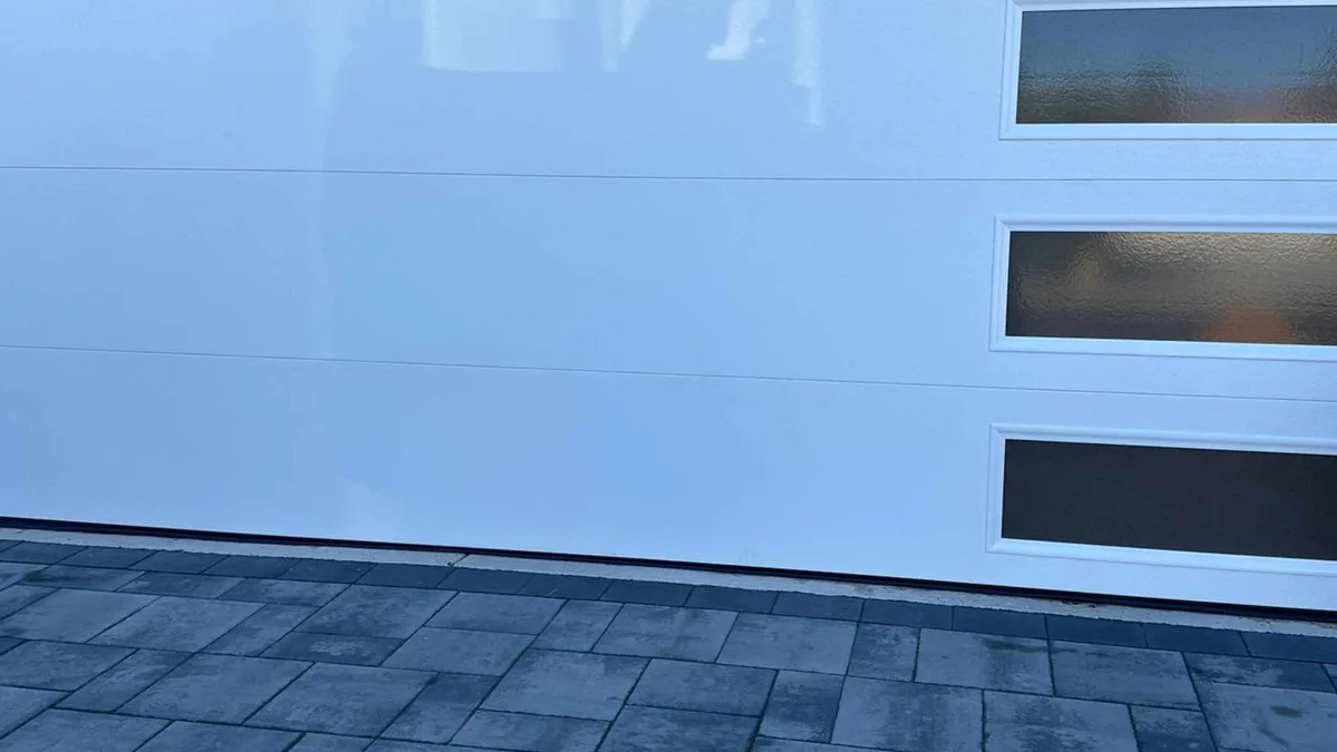 White garage door with three black-framed horizontal windows above a paver driveway